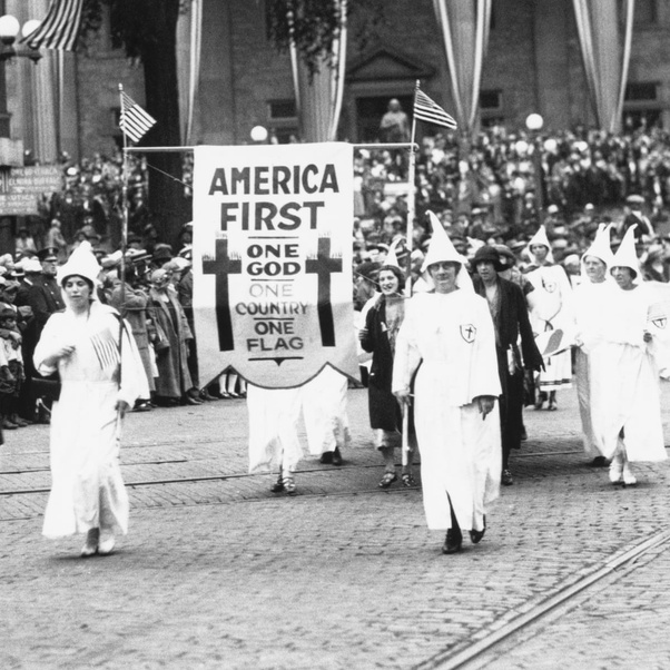 A bunch of Klansmen march down the street circa 
1922, carrying a banner that reads 'America First, One God, One Country, One Flag'
