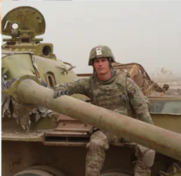 The candidate in full camouflage, with helmet, sitting on a tank