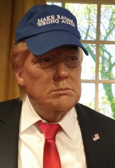 A wax figure that actually 
looks like Trump, wearing a blue baseball came that says 'Make Racism Wrong Again'