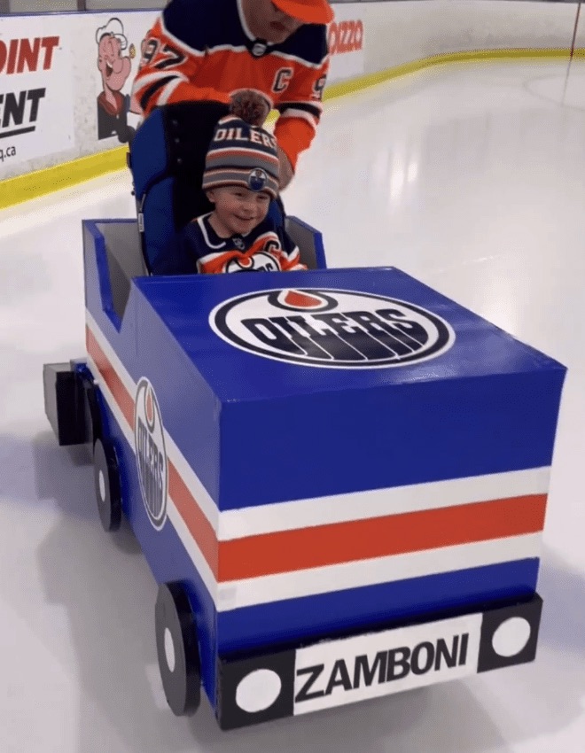 Father and son 
on the ice, with the son's wheelchair built into a mini-Zamboni machine with Oilers logo