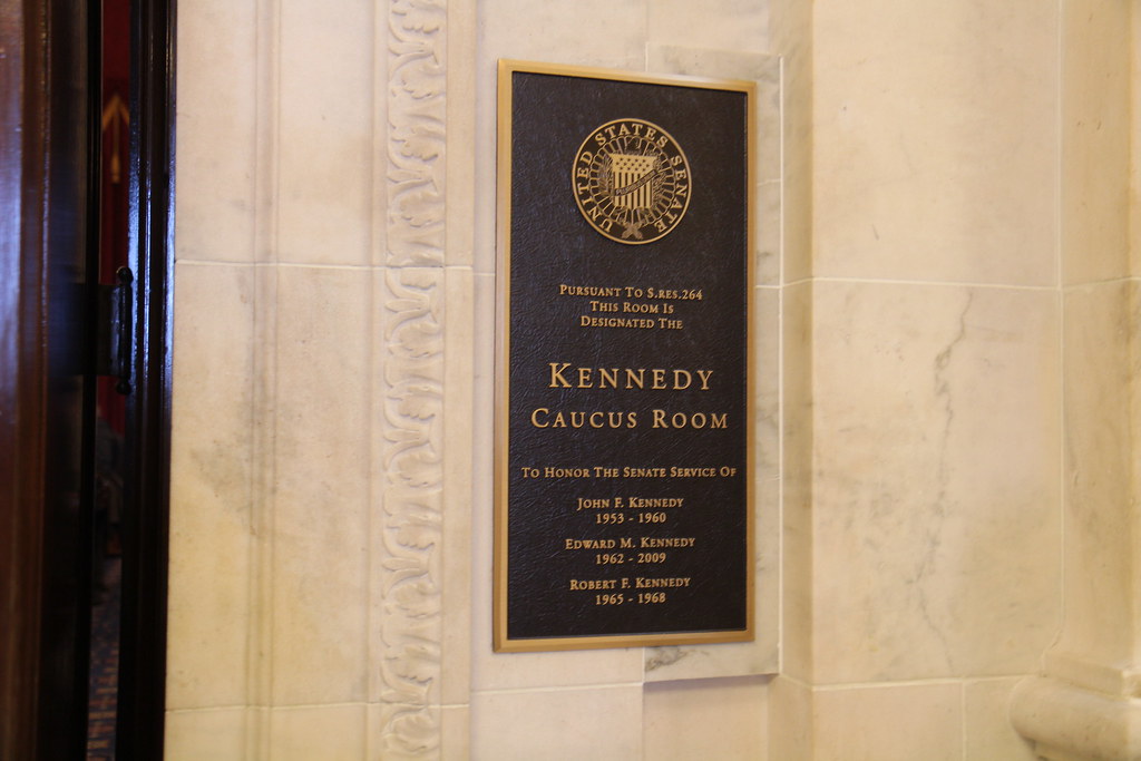 It says: 'Pursuant to Senate Resolution
264, this room is designated the Kennedy Caucus Room in honor of Senators John F. Kennedy, Robert F. Kennedy, and Edward Kennedy.'
It also lists their years of service in the Senate.