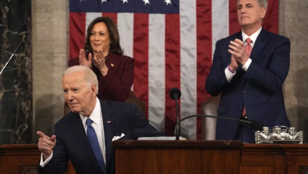 Biden points at the audience,
Kamala Harris is standing and applauding while smiling, Kevin McCarthy is standing and halfheartedly applauding while looking bored