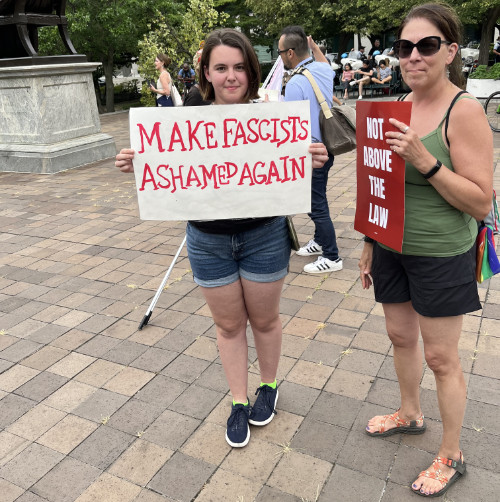 A woman holds a sign that says 'Make fascists ashamed again'