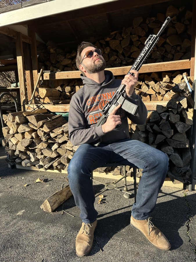 J.D. Vance, dressed in blue jeans
and a hoodie and aviator sunglasses points some sort of high-powered gun skyward