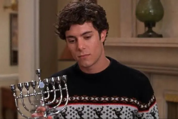 A teenager in a tacky holiday sweater holds a menorah