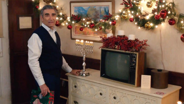A man in his sixties stands
next to a holiday display that includes garlands and a menorah