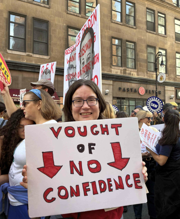 Her sign says
'VOUGHT OF NO CONFIDENCE'