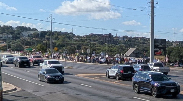 A large 
crowd lines one side of a street