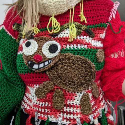 A crocheted sweater with a reindeer that is clearly meant to be Rudolph, but has crazy eyes