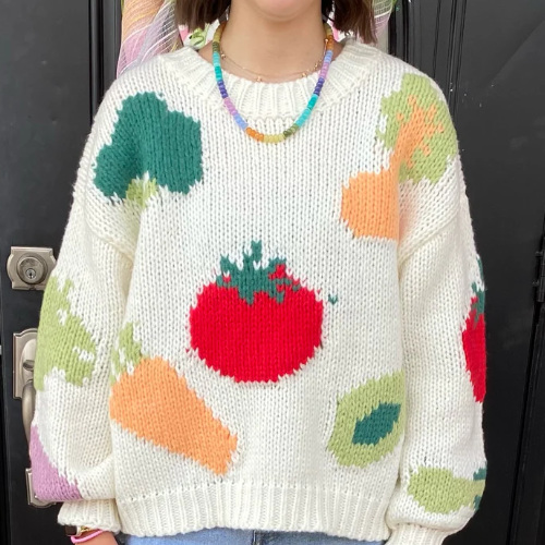 A white sweater with a bunch of giant, 3-D vegetables