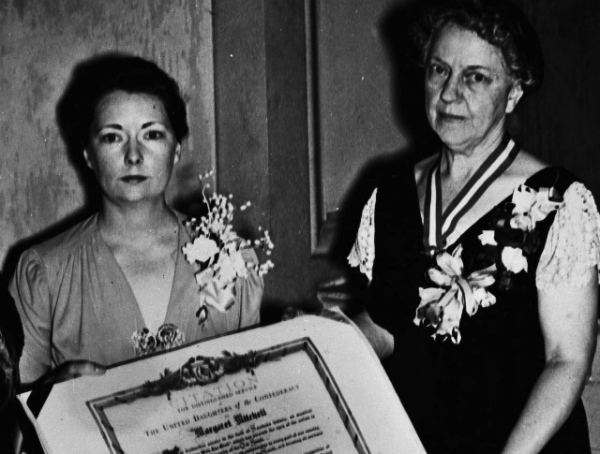 Black and white,
semi-blurry photo, of Margaret Mitchell getting a large, framed award from an elderly UDC member