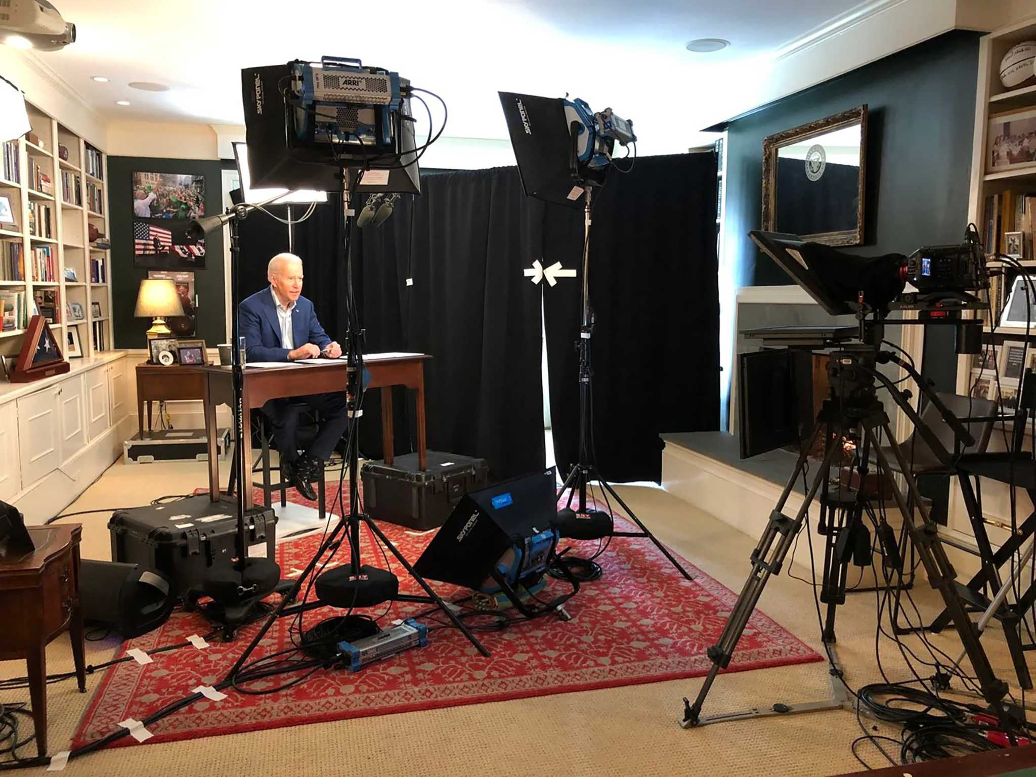 On the left wall is a bookcase, a desk
is placed at an angle to that, and then on the other side of the desk is a black drape that blocks light. Pointed at the desk,
with the bookcase as backdrop, is a camera and a couple of professional photographers' lights