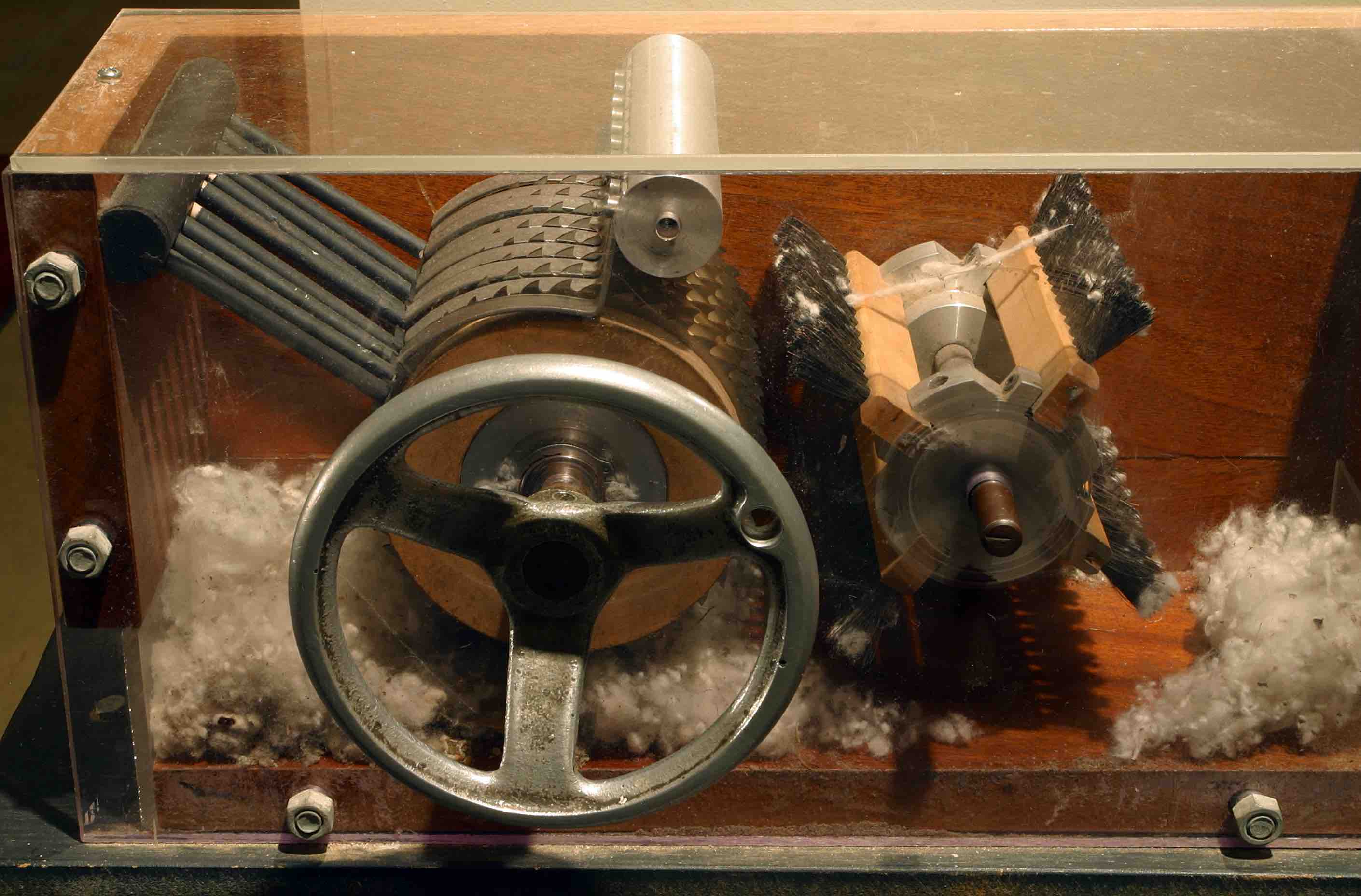 The cotton gin has multiple gears in it with
fairly sharp spokes, and a hand-turned wheel. As you feed cotton in on one side, and turn the wheel, it pulls the cotton through the
gears/spokes, and separates out seeds