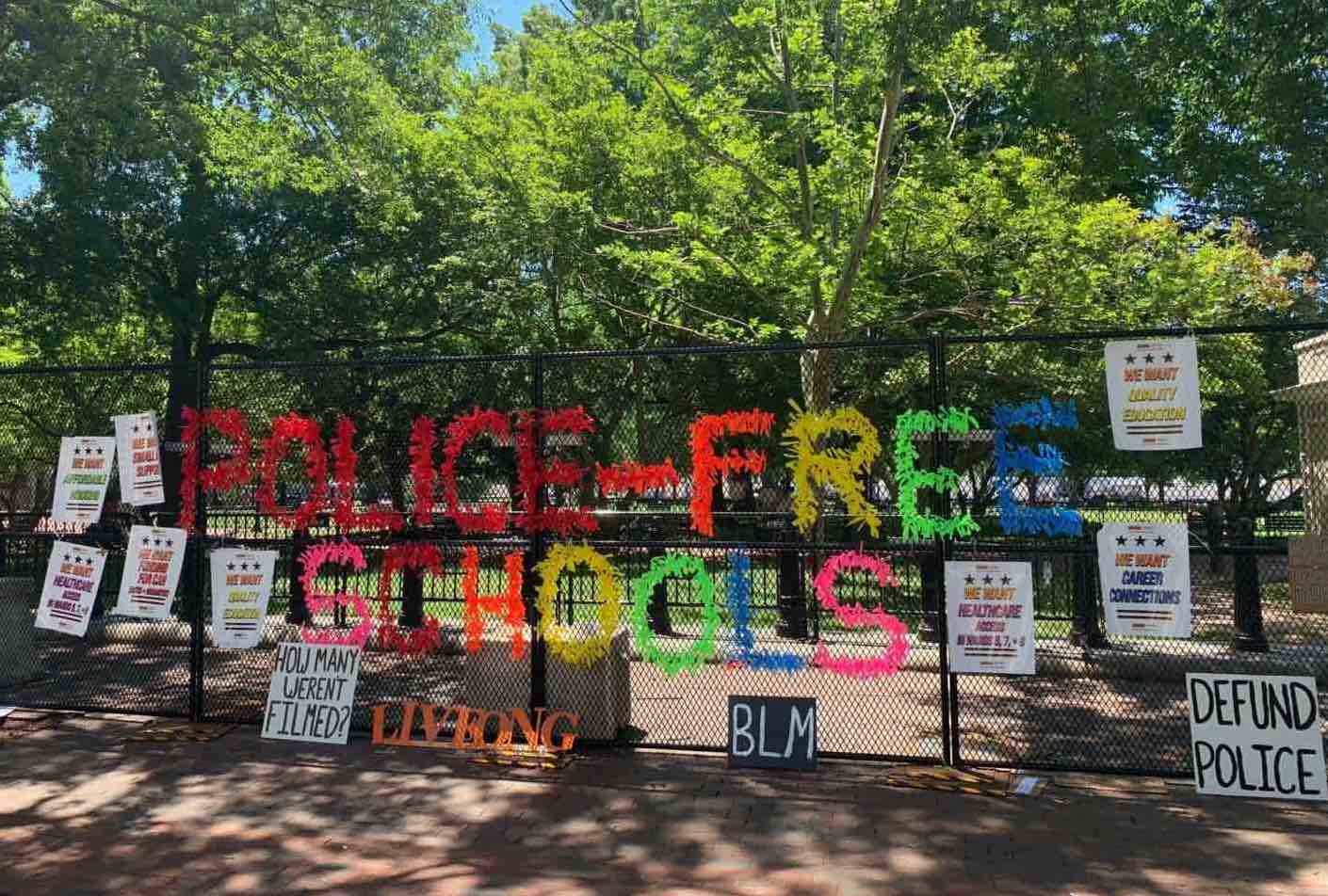 The phrase 'police-free schools' is spelled out in
large colorful letters made out of hundreds of tied ribbons, and then surrounded by anti-police placards