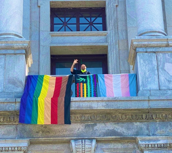 John Fetterman standing next to
the LGBTQ+ and pro-marijuana flags that fly outside his office