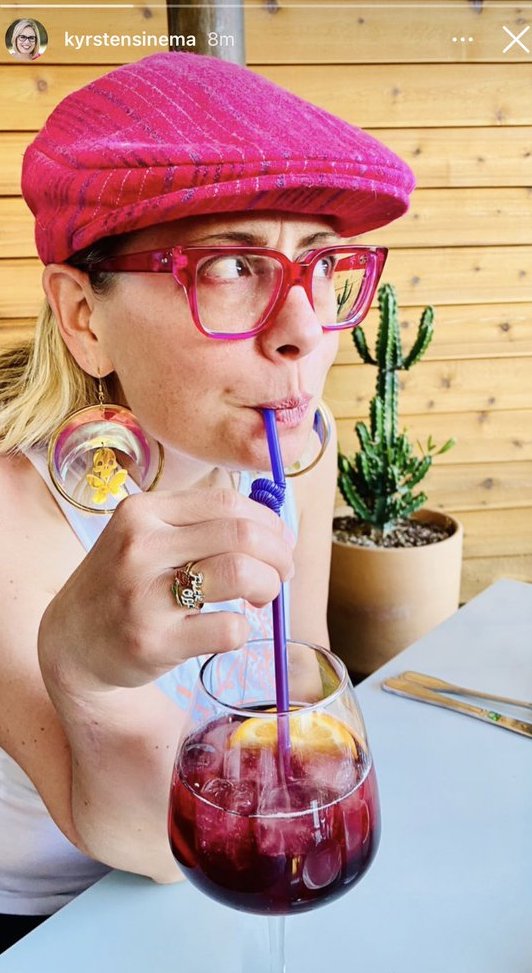Sinema is looking into the distance, drinking
a sangria, wearing a pink cab driver hat and fuchsia glasses, and is quite clearly displaying a ring on her right ring finger that says
'fuck off'