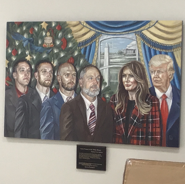 A very mediocre oil 
painting that shows Donald and Melania Trump, apparently in the Oval Office, along with four men in suits, and 
what looks like a Christmas tree. There is a plaque beneath the painting.