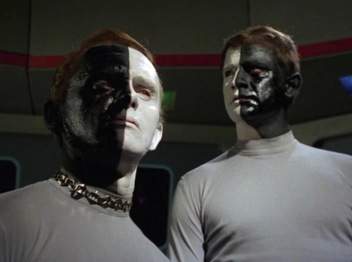 Two characters, one with a face that is black
on the left and white on the right and one with a face that is white on the left and black on the right
