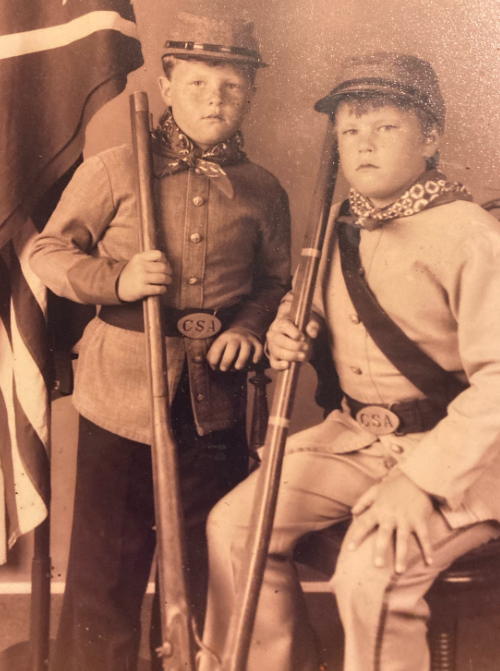 (Z) sitting, next to
his brother, who is standing. Both are dressed in CSA uniforms, with a Confederate flag in the background.