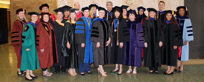A bunch of professors wearing gowns that
are black, or black with colored trim, or green, or purple, or crimson, or light blue