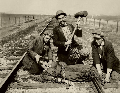 Three mustachioed men tie a 
damsel in distress to train tracks