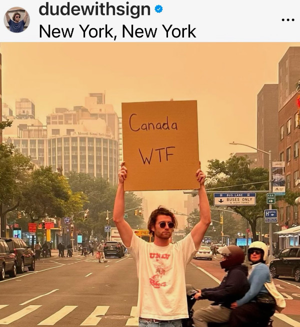 A man surrounded by smoke
from the wildfires holds up a sign that says 'Canada, WTF?'