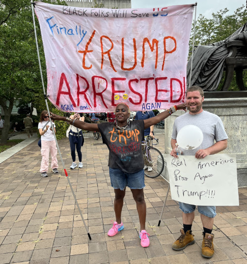 A Black woman has a banner that says 'Black folks will save us' and 'Finally, Trump arrested again... and again