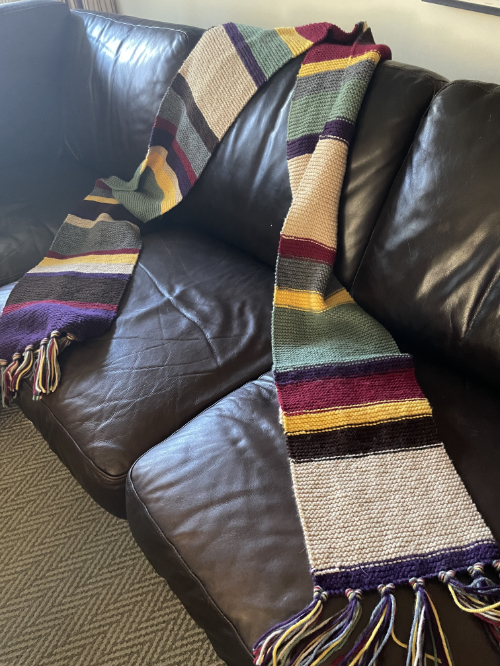 A scarf, primarily in beige
and green, that is draped on a leather couch, and must be at least 10 feet long