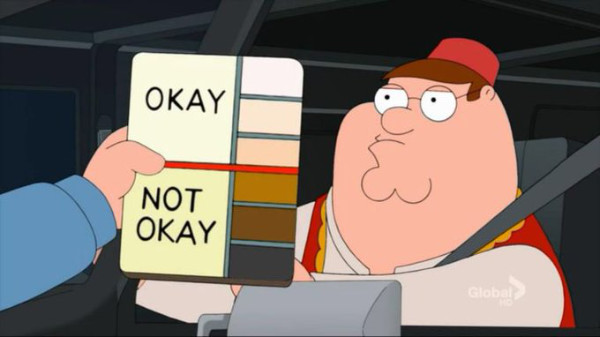 A person holds up
a card with six different skin colors, from pale white to dark brown. The first three, which a white person 
might have, are 'OKAY,' while the other three are 'NOT OKAY'