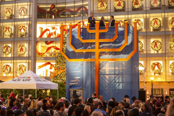 A very large menorah in front of a brightly lit building; there are also rainbows visible