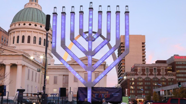 A large menorah; through it you can see a government building and an arch