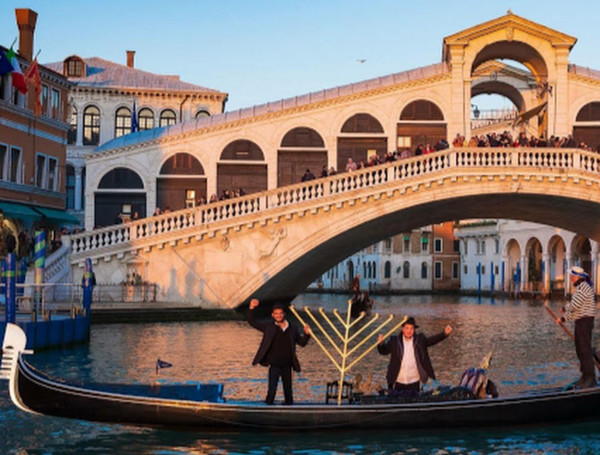 Two Jewish men in a gondola with a menorah pass by a covered bridge