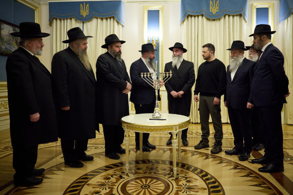 8 rabbis and a man in black turtleneck and military pants light a menorah
