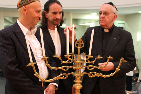 Three men light a menorah, one of them is a very familiar-looking Catholic priest, with black suit and cleric's collar