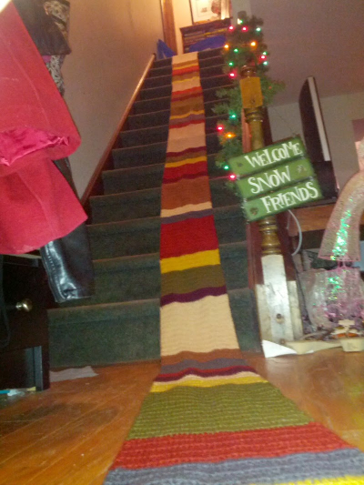 A multicolor scarf starts at the top of the staircase, 
goes all the way down, and runs along the floor enough that the camera cannot capture it all; the total must be at least 30 feet