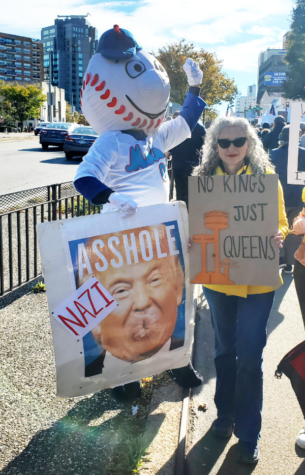 A person dressed as New 
York Mets mascot Mr. Met holds a sign that says 'Nazi Asshole' and had Donald Trump's head but with the mouth replaced
by an anus. He is standing next to a woman whose sign reads 'No Kings Only Queens.'