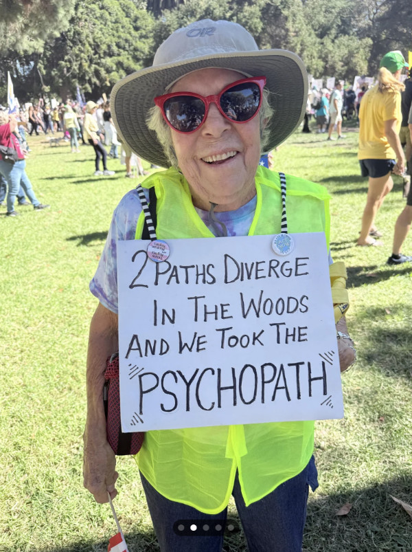 A woman holds 
a sign that says '2 PATHS DIVERGE IN THE WOODS AND WE TOOK THE PSYCHOPATH.'