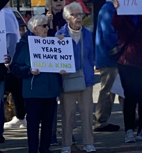 Two women, who are both pushing
100, hold a sign that says 'In our 90+ years, we have not had a king.'