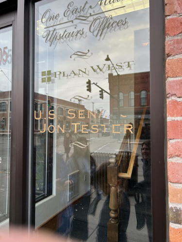 A glass door leading
into an office park has logos for a bank, an insurance agency, and Tester; the letters in Tester's name are 
peeling off