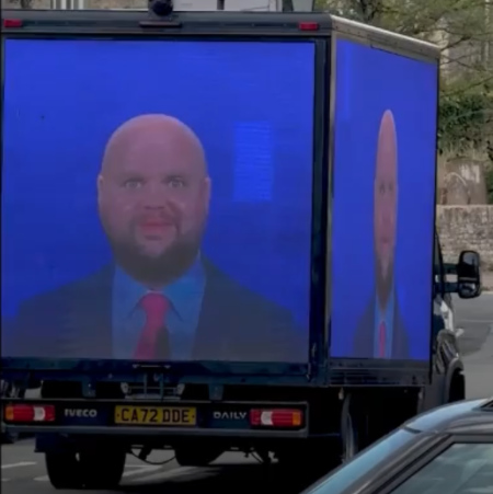A box truck with video screens on three sides, all of them showing the photo of vance as a bald man with bulging eyes