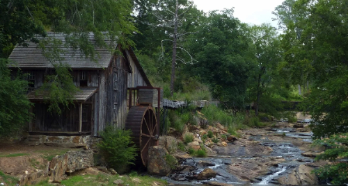 A rustic cabin, with a water wheel, next to a stream