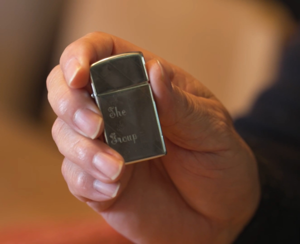 A hand holding
a Zippo lighter with 'The Group' engraved on it