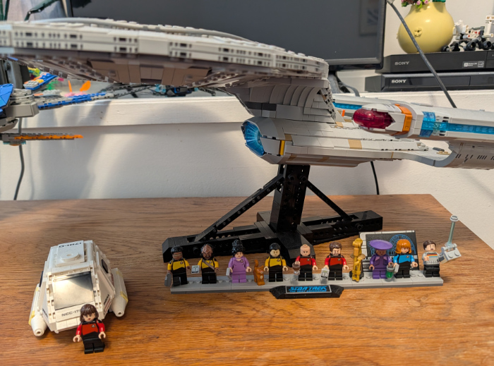 There is the Enterprise and also a shuttle.
Ro is standing next to the shuttle, and then standing under the Enterprise, in order, are Geordi, Worf, Troi, Data, Picard, Riker, Guinan,
Beverly Crusher and Wesley.