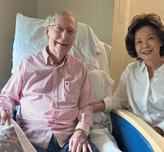 McConnell is sitting in a
hospital bed in blue jeans and a checked shirt and holding a newspaper, while Chao is standing next to him