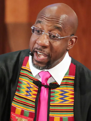 Warnock preaching, while wearing a pink tie and an African-themed vest