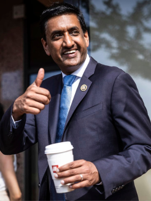 Khanna striding along a street in D.C. turning to look back at the photographer, and flashing a smile and a thumbs
up while holding a coffee cup in his other hand.