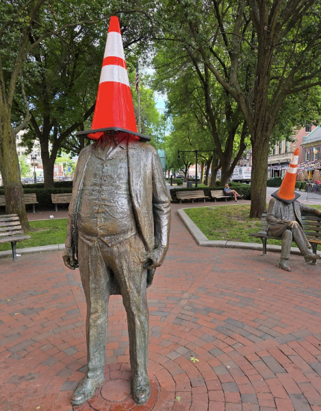 A bronze statue of a man in a suit,
with a traffic cone covering his entire head and face