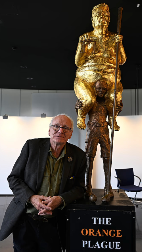 A base with the title
'THE ORANGE PLAGUE,' and then 8-1/2 feet of sculpture, with a gold-colored, obese Trump sitting on the shoulders of a
much thinner and smaller bronze-colored man.